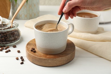 Photo of Woman stirring coffee with spoon at white wooden table, closeup