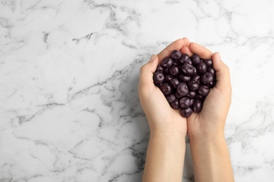 Photo of Top view of woman holding fresh acai berries on marble background, closeup. Space for text