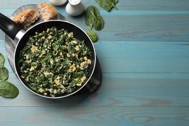 Photo of Tasty spinach dip with eggs in dish served on light blue wooden table, flat lay. Space for text