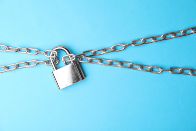 Photo of Steel padlock and chains on light blue background, top view. Safety concept
