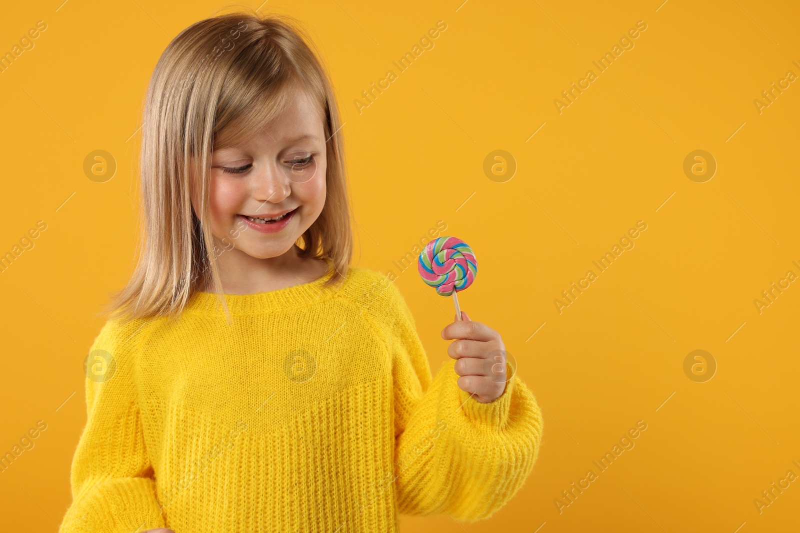 Photo of Happy girl with lollipop on orange background. Space for text