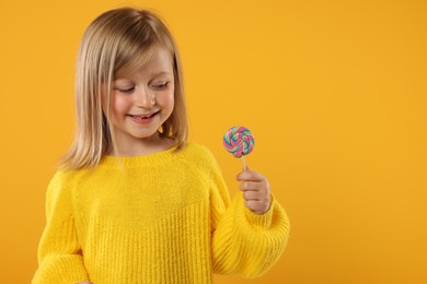 Photo of Happy girl with lollipop on orange background. Space for text