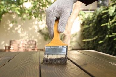 Photo of Man applying wood stain onto wooden surface outdoors, closeup