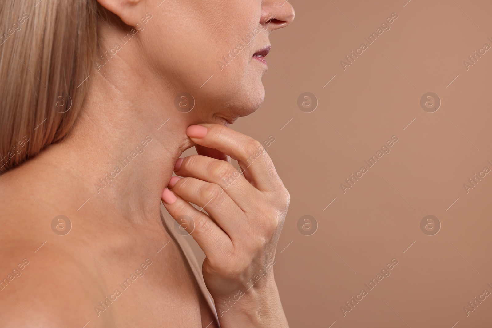 Photo of Mature woman touching her neck on beige background, closeup. Space for text