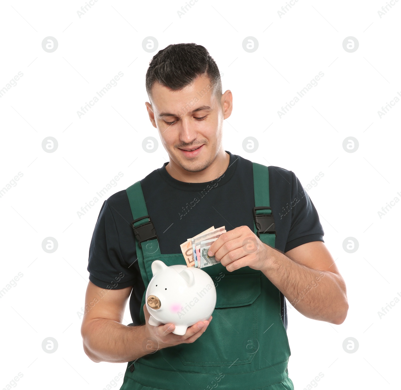 Photo of Portrait of male worker in uniform putting money into piggy bank on white background