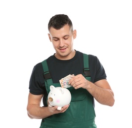 Portrait of male worker in uniform putting money into piggy bank on white background