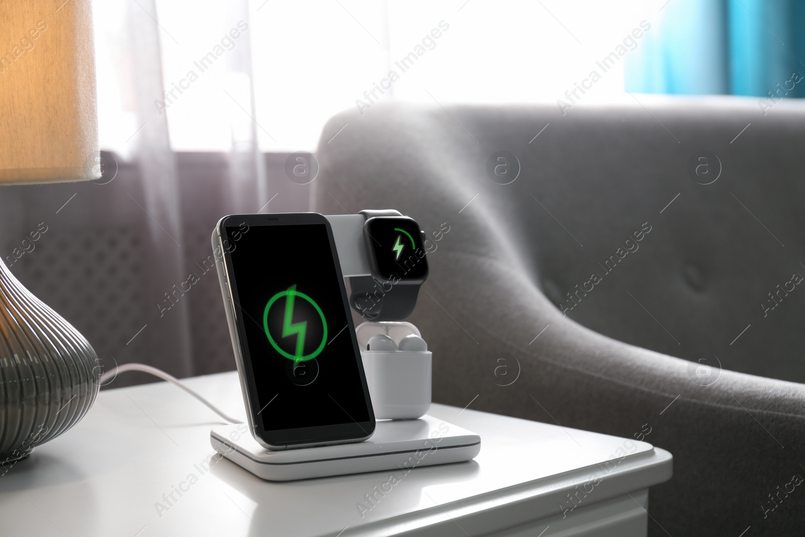 Photo of Smartphone, watch and earphones charging on wireless pad in room. Space for text