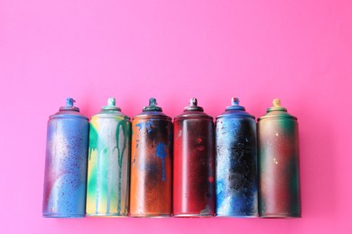 Photo of Many spray paint cans on pink background, flat lay