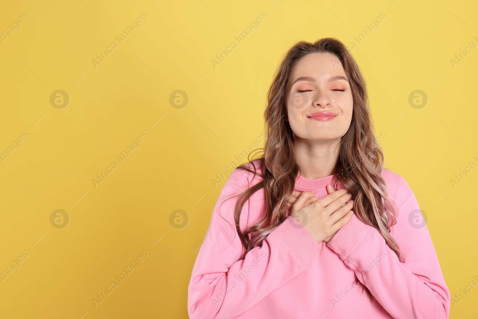 Photo of Beautiful grateful woman with hands on chest against yellow background. Space for text