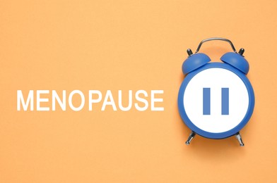 Menopause word and alarm clock with pause symbol on orange background, top view