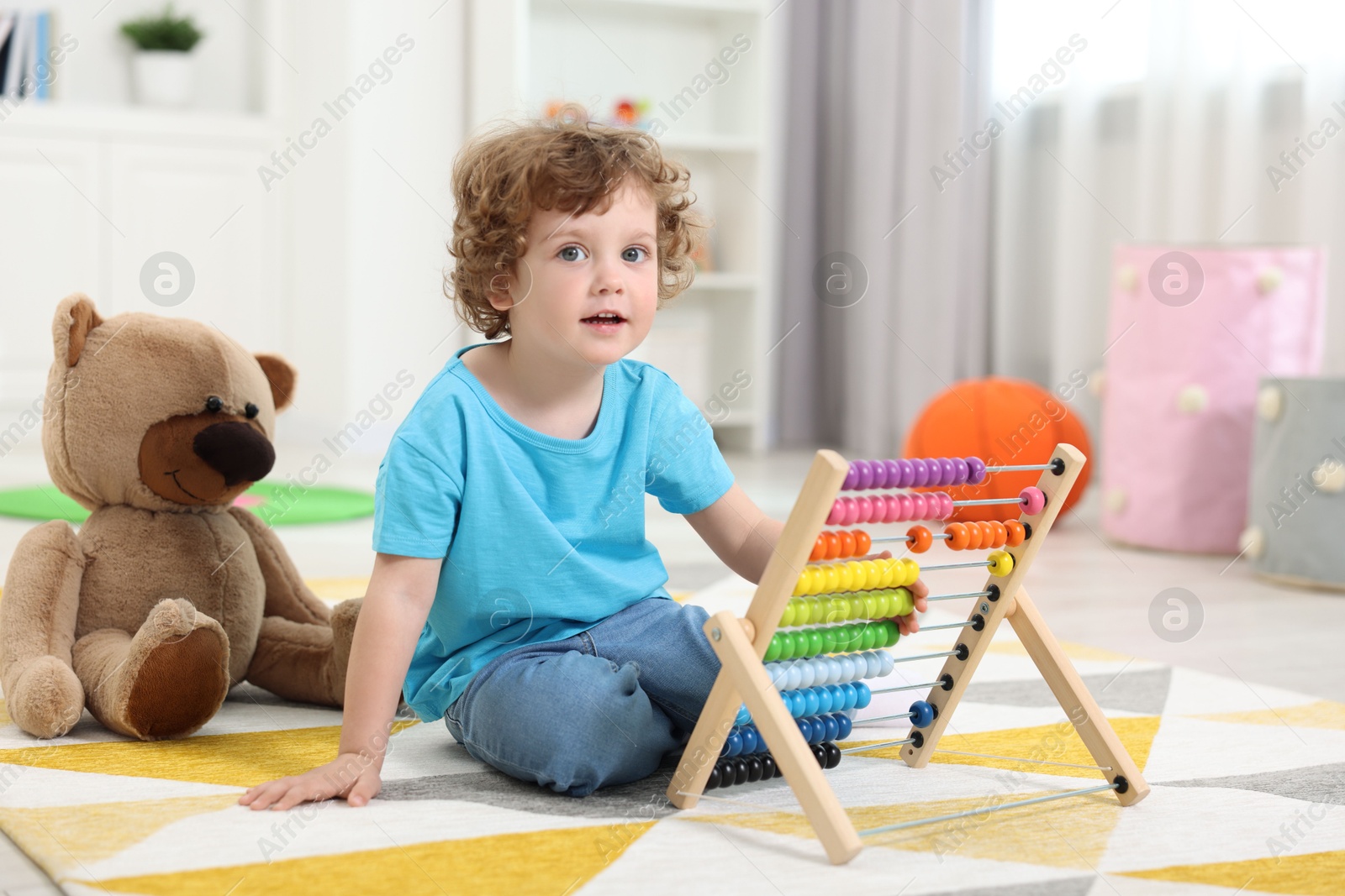 Photo of Cute little boy playing with wooden abacus on floor in kindergarten