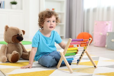 Photo of Cute little boy playing with wooden abacus on floor in kindergarten