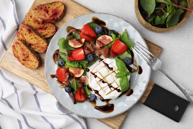 Delicious salad with brie cheese, prosciutto, berries and balsamic vinegar served on light grey table, flat lay