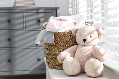 Photo of Wicker laundry basket with different clothes and teddy bear on window sill indoors. Space for text