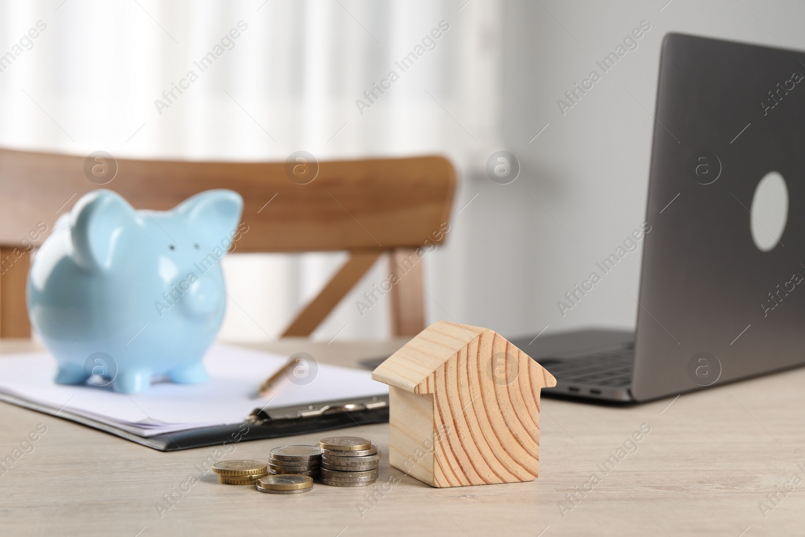 Photo of House model, coins, piggy bank and laptop on wooden table indoors, selective focus