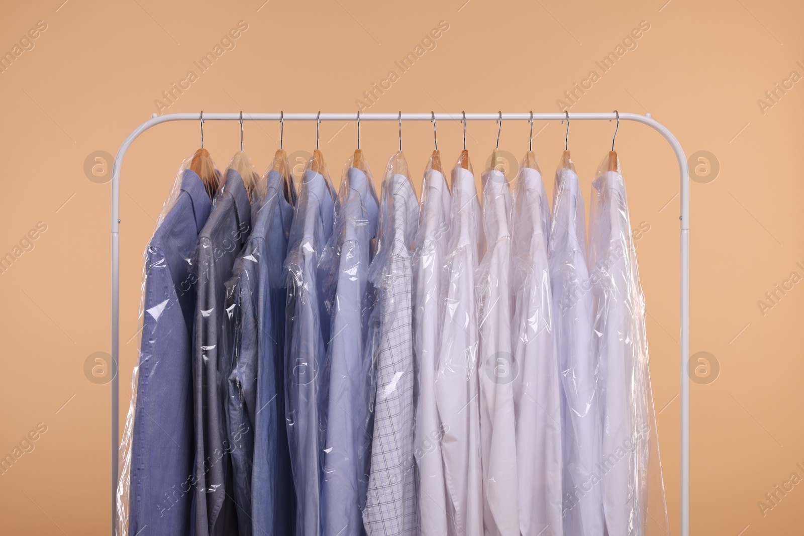 Photo of Dry-cleaning service. Many different clothes in plastic bags hanging on rack against beige background