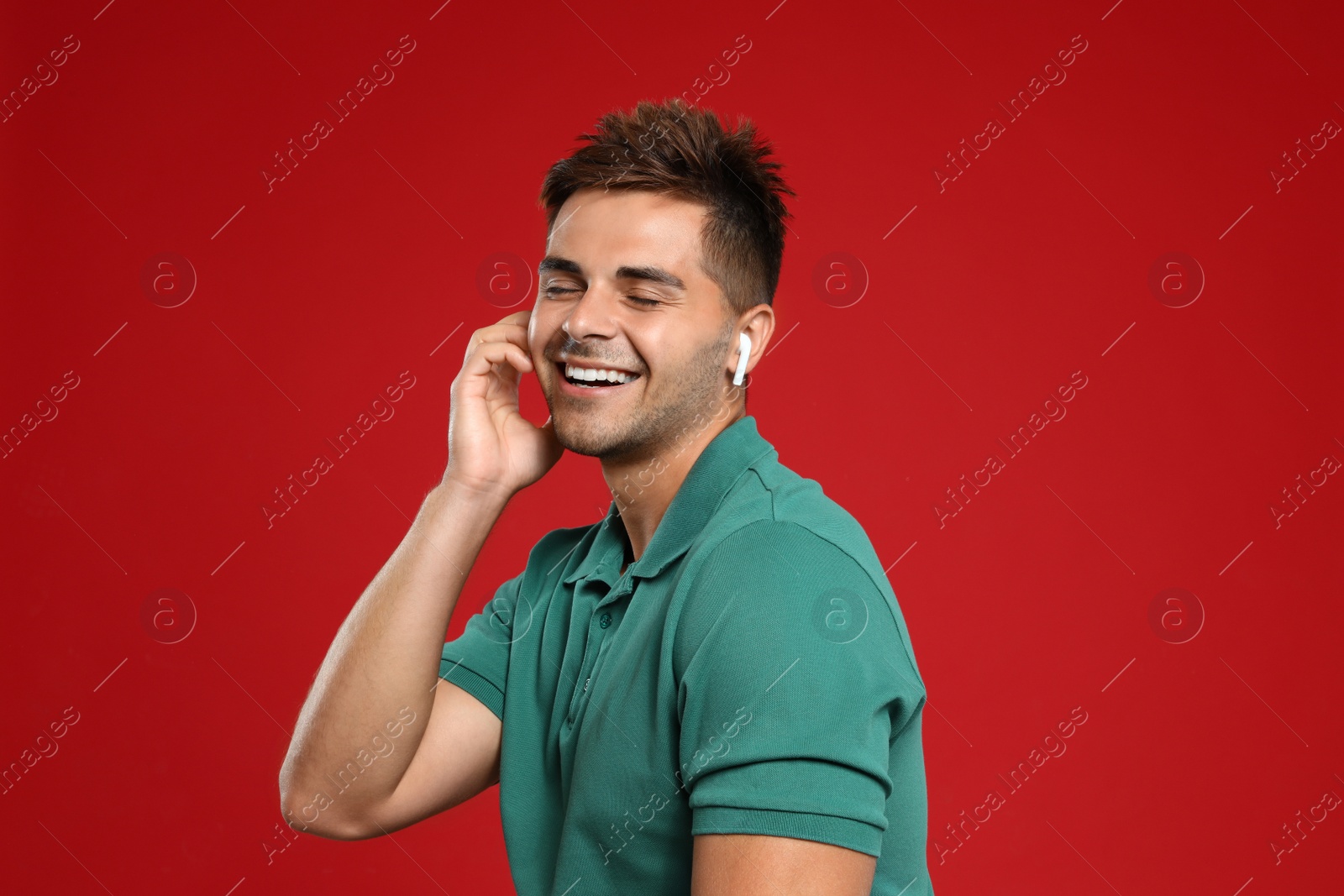 Photo of Happy young man listening to music through wireless earphones on red background
