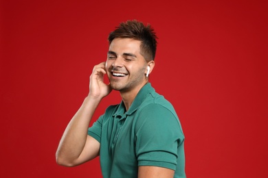 Happy young man listening to music through wireless earphones on red background