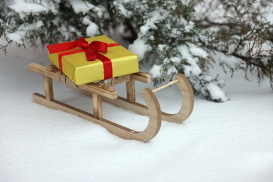 Photo of Wooden sleigh with gift box on snow outdoors