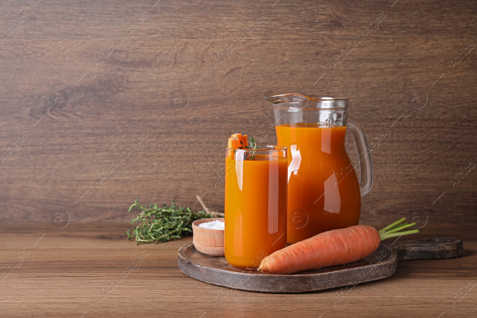 Photo of Freshly made carrot juice on wooden table, space for text