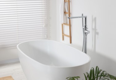 Stylish bathroom interior with ceramic tub and terry towel on wooden shelf