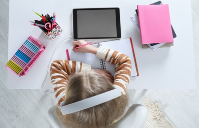 Photo of Cute little girl with modern tablet studying online at table, top view. E-learning