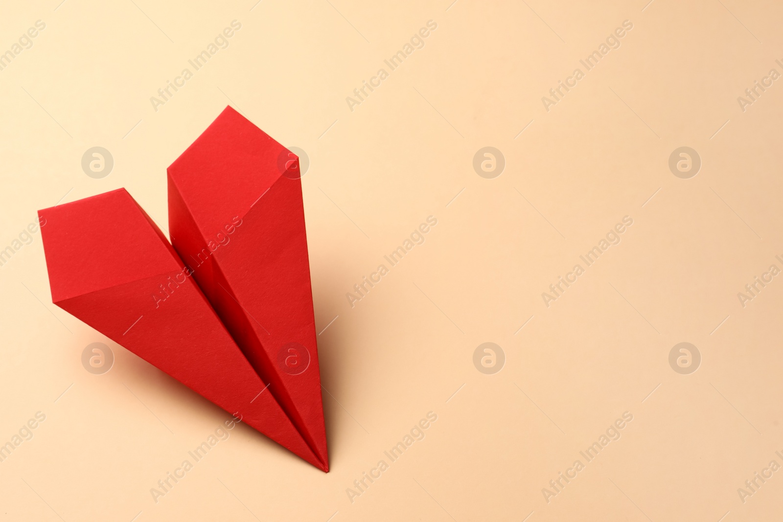 Photo of Handmade red paper plane on beige background, space for text