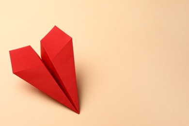 Photo of Handmade red paper plane on beige background, space for text