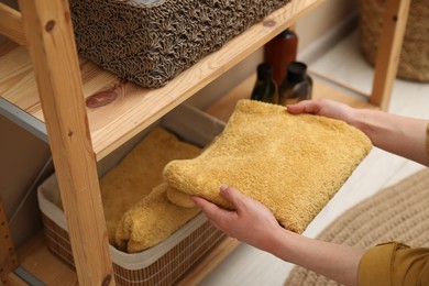 Woman putting towel into storage basket indoors, closeup