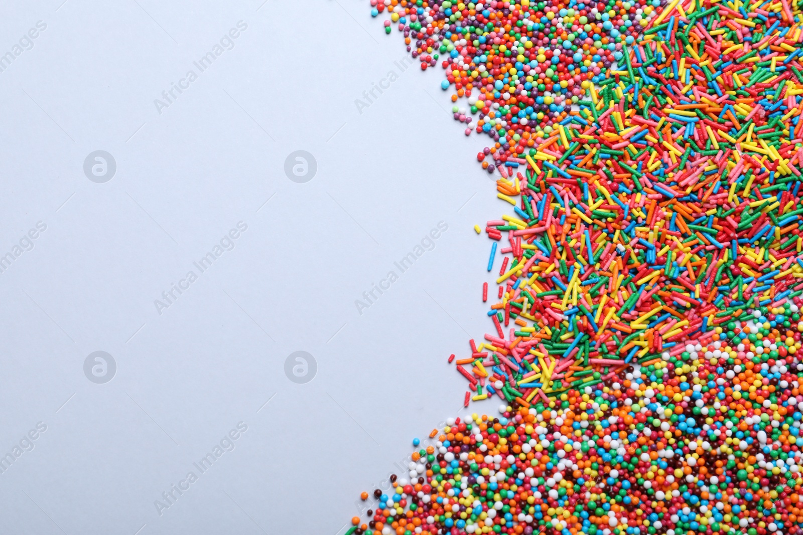 Photo of Colorful sprinkles on light grey background, flat lay with space for text. Confectionery decor