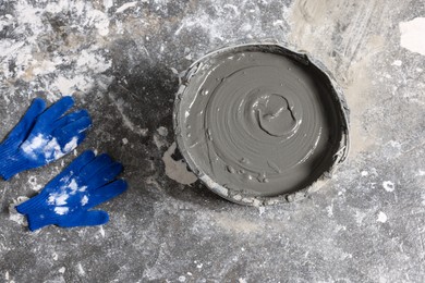 Photo of Bucket of concrete and gloves on floor indoors, flat lay