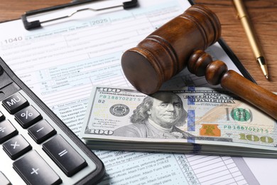 Photo of Tax return form, dollar banknotes, gavel, pen and calculator on wooden table, closeup