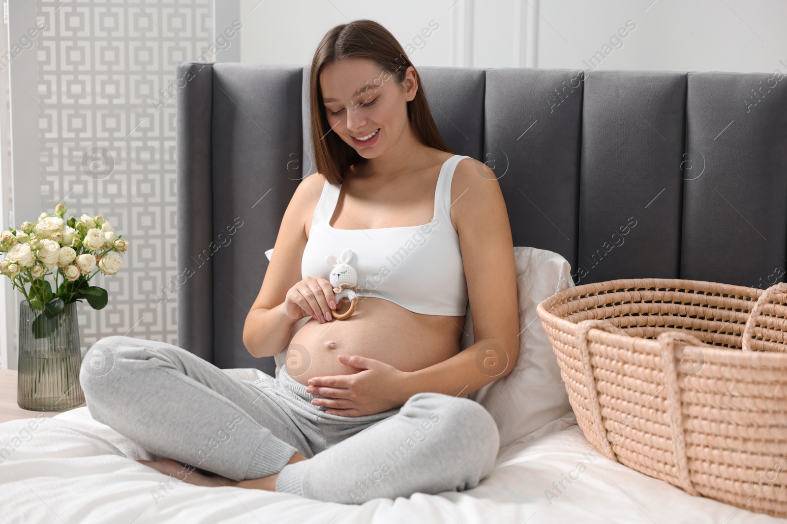 Photo of Beautiful pregnant woman with bunny toy sitting on bed indoors