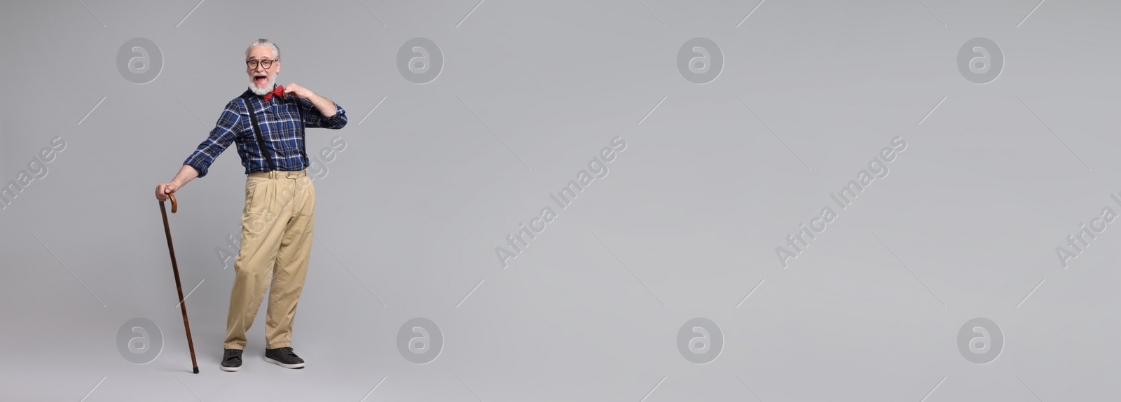 Image of Cheerful senior man with walking cane on gray background. Banner design with space for text