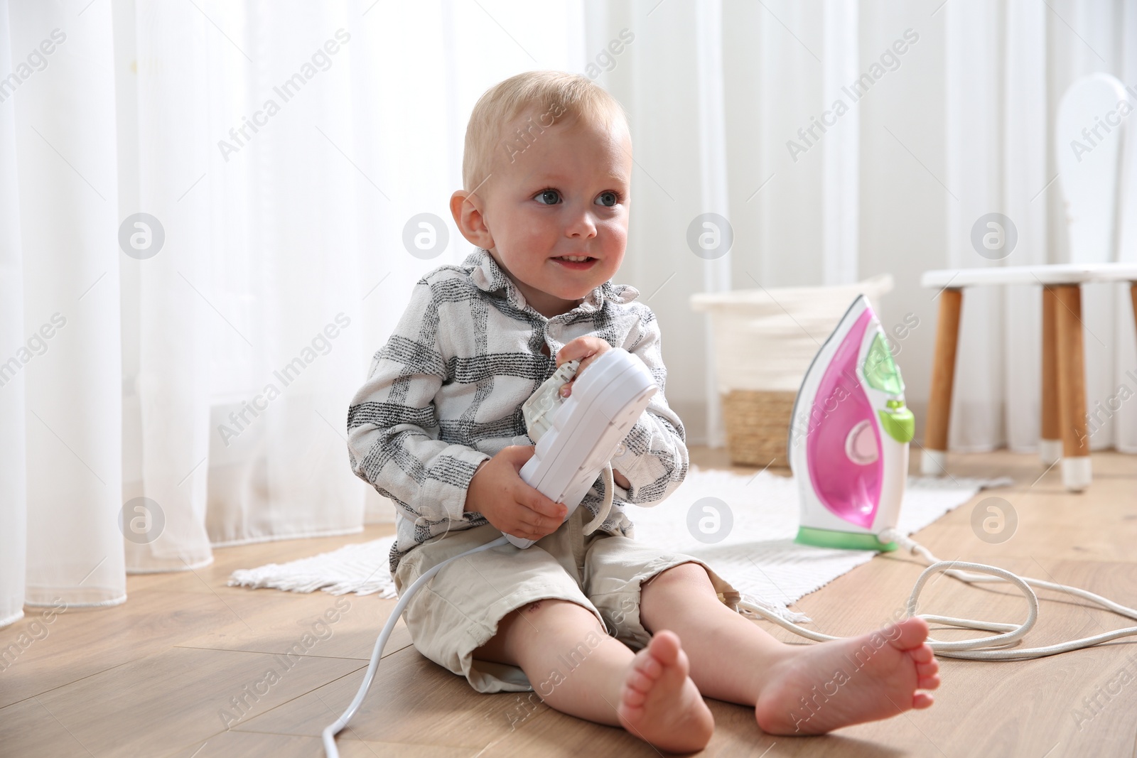 Photo of Little child playing with power strip and iron plug on floor at home. Dangerous situation