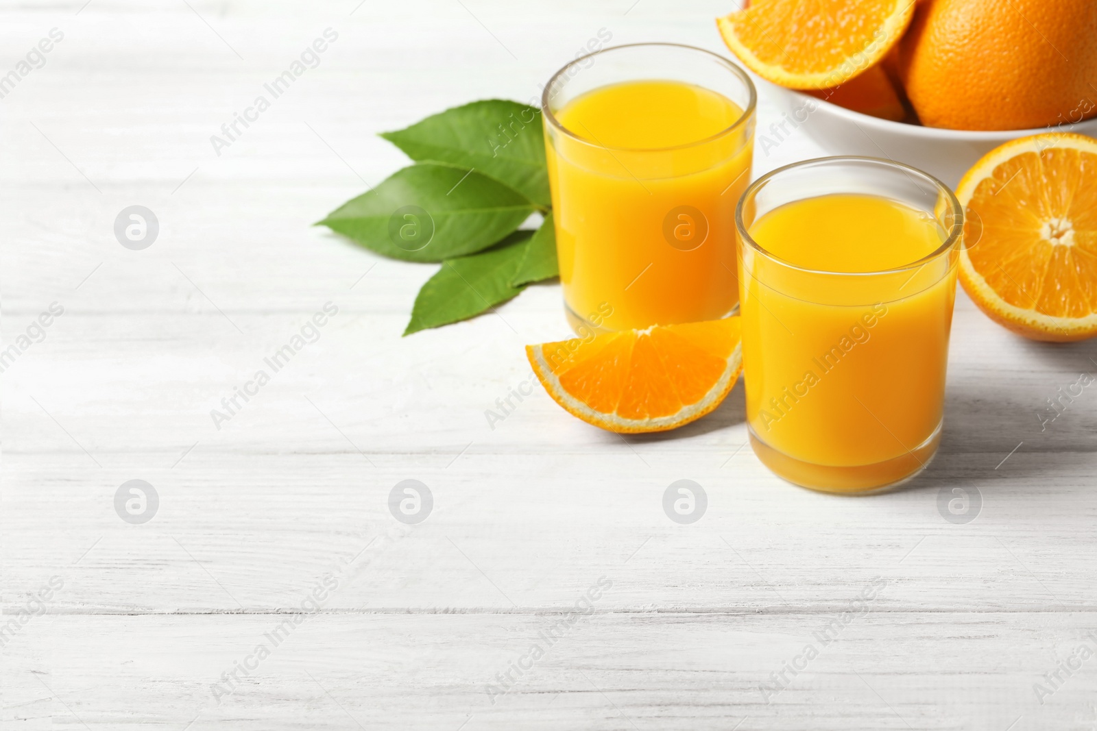 Photo of Glasses of orange juice and fresh fruits on white wooden table. Space for text