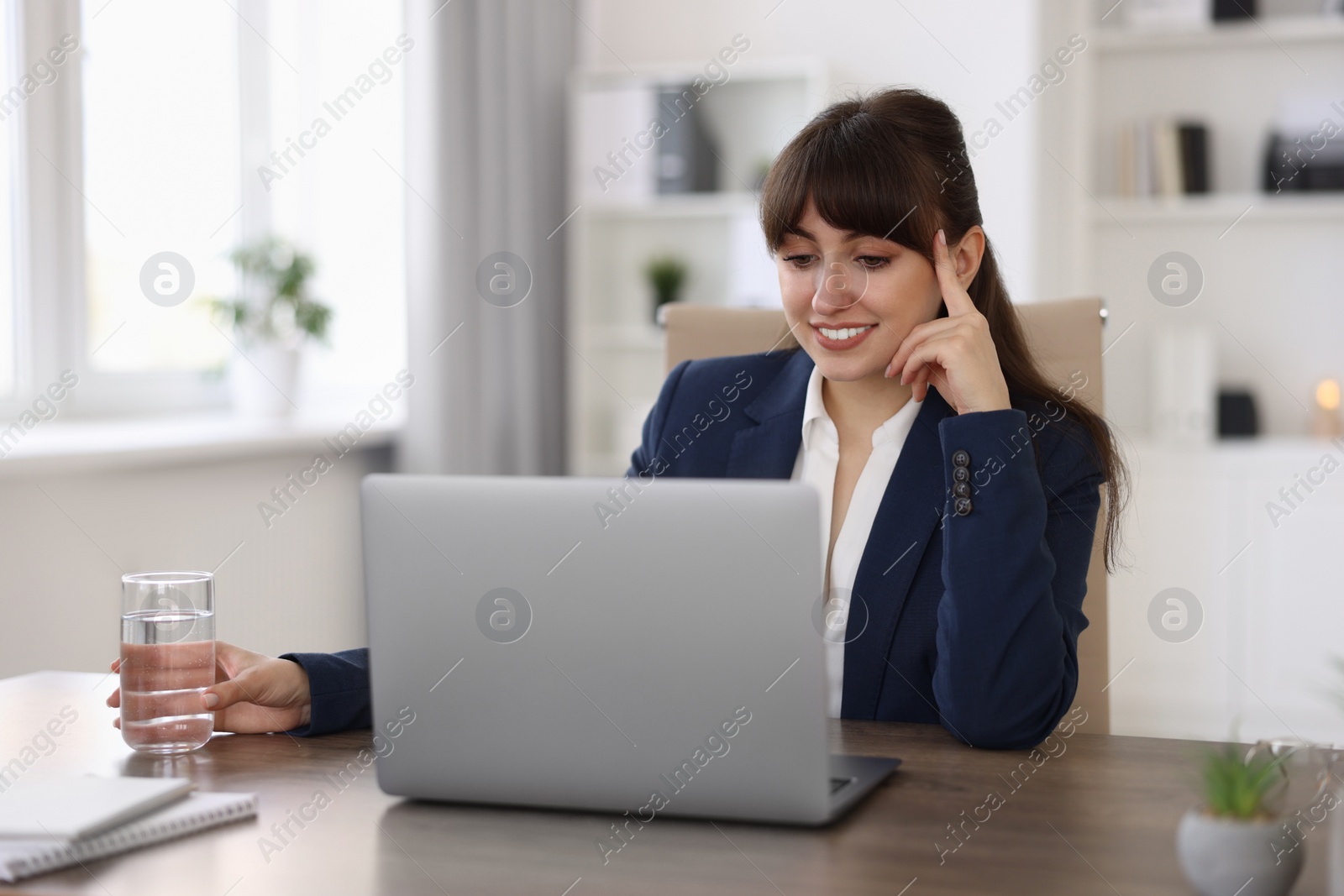 Photo of Woman with glass of water watching webinar at wooden table in office