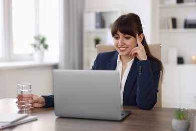 Woman with glass of water watching webinar at wooden table in office