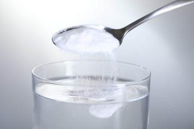 Photo of Adding baking soda into glass of water on light grey background, closeup