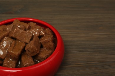Photo of Wet pet food in feeding bowl on wooden background, closeup. Space for text