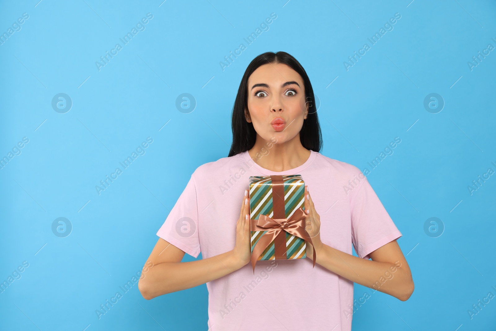 Photo of Emotional young woman holding gift box on light blue background