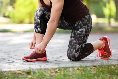 Photo of Young woman tying shoelaces before running in park, focus on legs