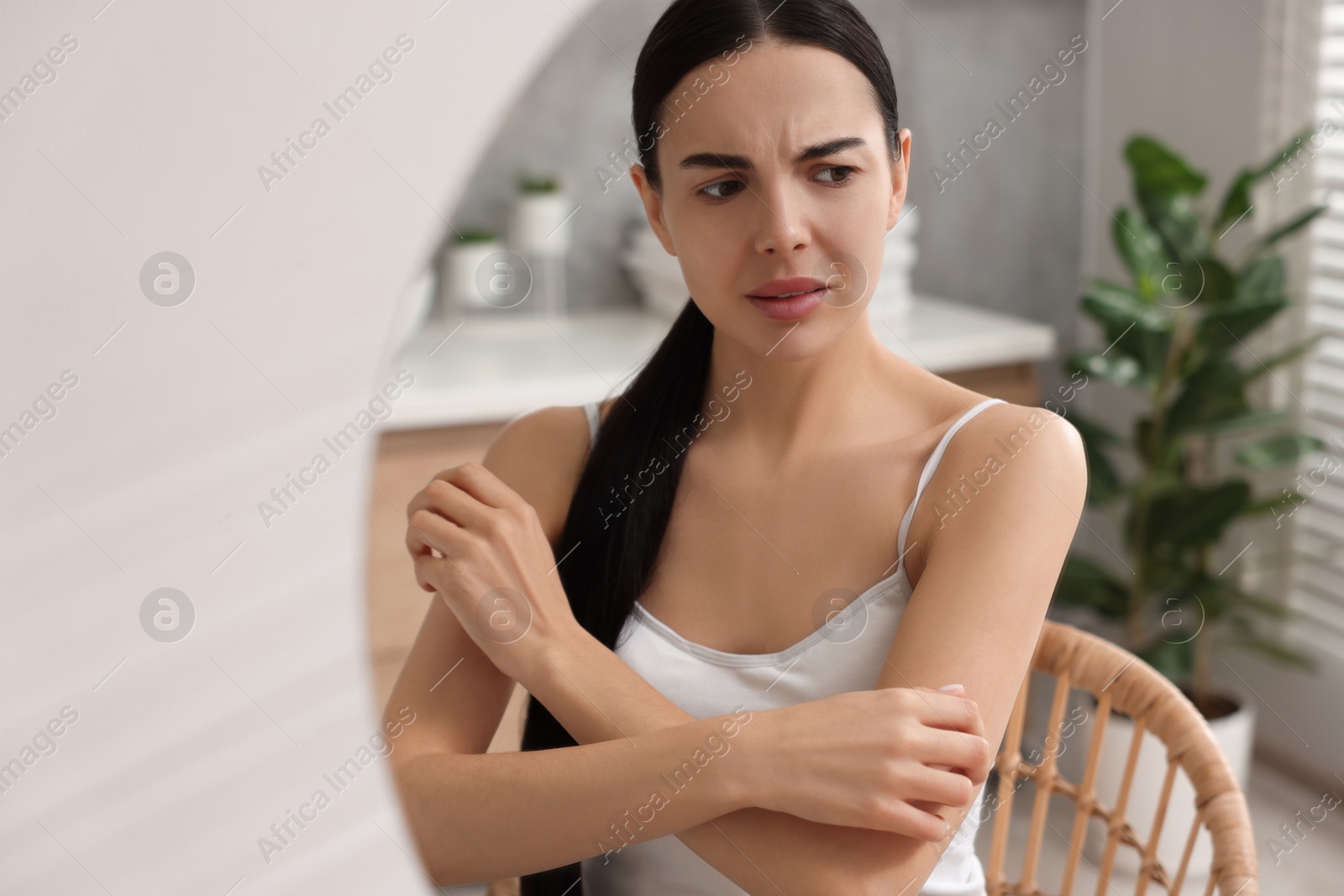 Photo of Woman with dry skin looking at mirror in bathroom