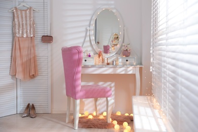 Elegant dressing table with lights and pink chair in stylish room interior