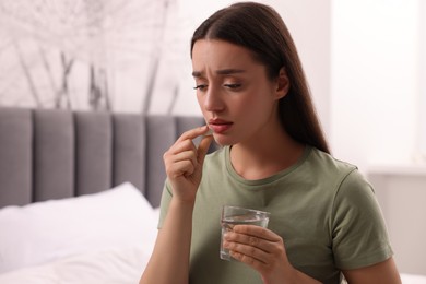 Photo of Depressed woman with glass of water taking antidepressant pill on bed indoors, space for text