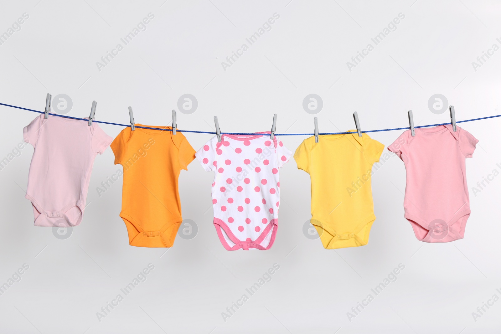 Photo of Colorful baby onesies drying on laundry line against light background