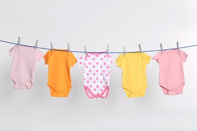 Photo of Colorful baby onesies drying on laundry line against light background