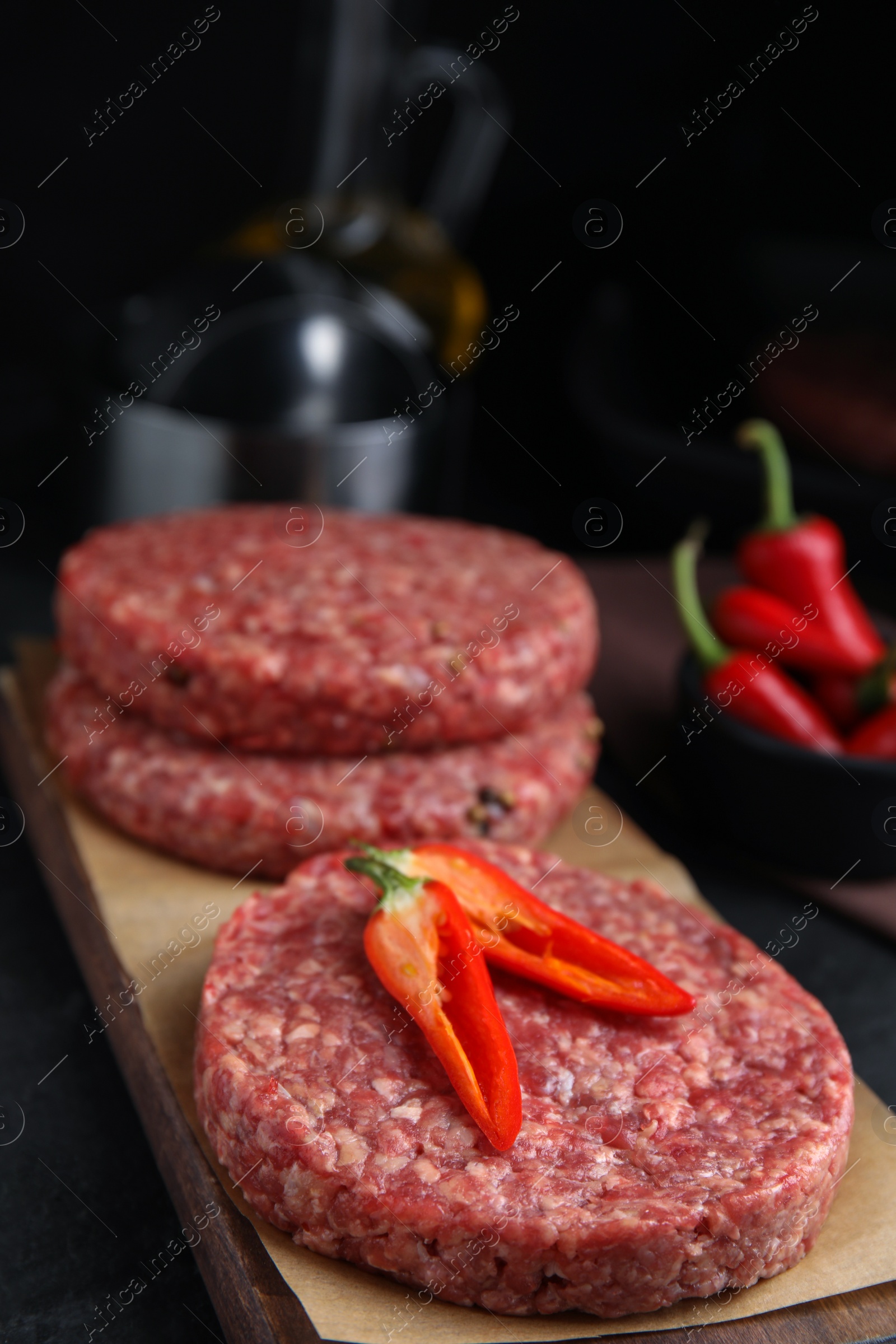 Photo of Raw hamburger patties with chili pepper on black table, closeup