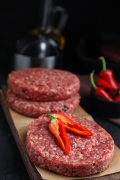 Photo of Raw hamburger patties with chili pepper on black table, closeup