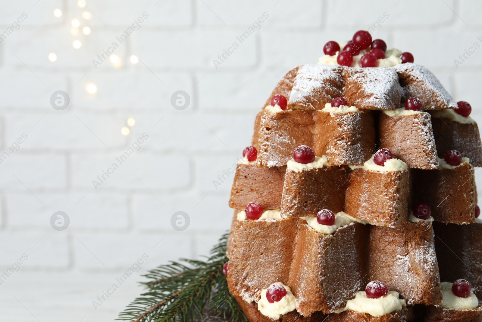 Photo of Delicious Pandoro Christmas tree cake with powdered sugar and berries on white table near brick wall, closeup. Space for text